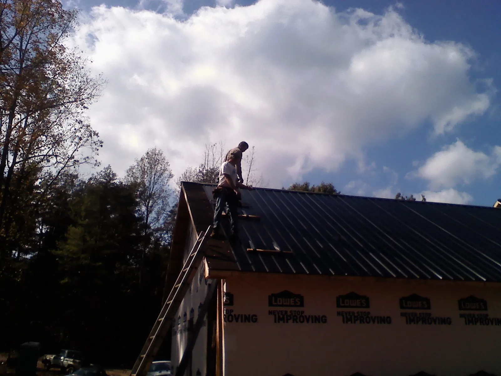 Roofer fastening dark metal panels high against a cloudy sky, from a Roof Inspection job in Prospect